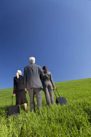Concept shot showing three business executives, one male and two female, walking through a green field towards the horizon. Environmental, business and travel concepts, shot on location.の写真素材