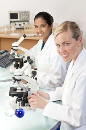 A female Asian medical or scientific researcher or doctor using her microscope in a laboratory with her colleague out of focus in the foreground.の写真素材
