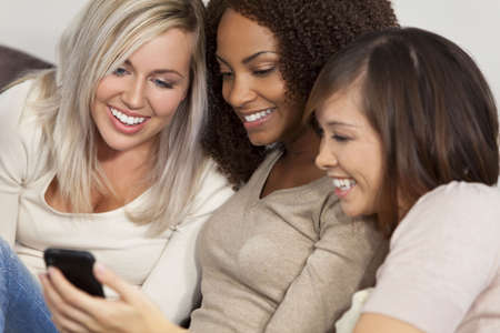 Three beautiful young women having fun looking at something funny on their smart cell phone and laughingの写真素材