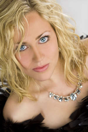 Studio shot of a beautiful blond haired blue eyed female model wrapped in black feathers and wearing a necklaceの写真素材