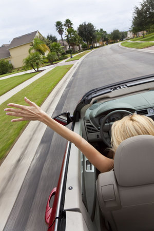 A beautiful young blond woman driving her convertible car with her hand in the air feeling the wind...