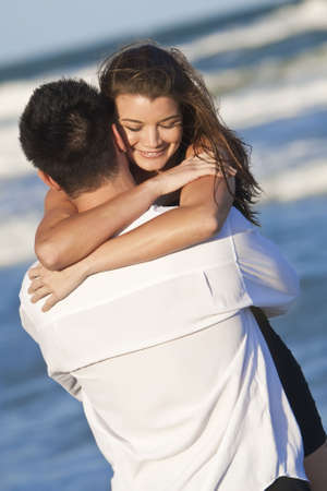 A young man and woman happy having fun and embracing as a romantic couple on a beach の写真素材