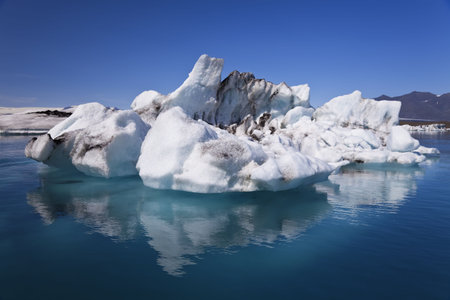 A glacial iceberg and its symmetrical reflection floating on the Iceberg Lagoon, Jokulsarlon,...