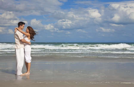 A young man and woman embracing as a romantic couple on a beach with a bright blue sky, shot with copy space.の写真素材