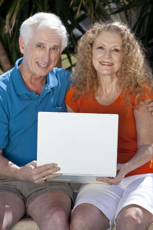 A senior retired man and woman couple sitting outside using a wireless laptop computer to surf the internet.の写真素材