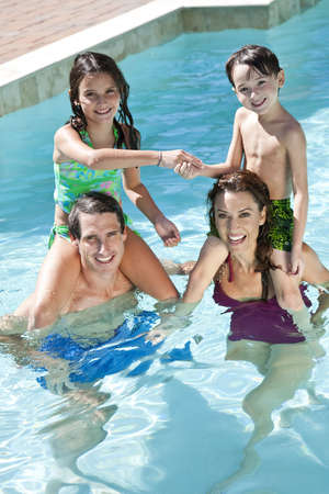 A mother and father having fun on vacation playing with their children on their shoulders in a swimming poolの写真素材