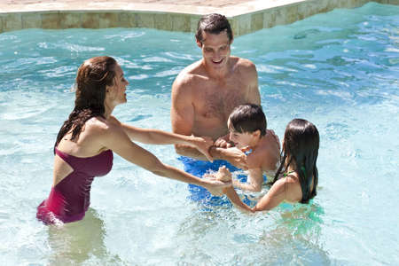 A mother and father having fun on vacation playing with their children on their shoulders in a swimming poolの写真素材