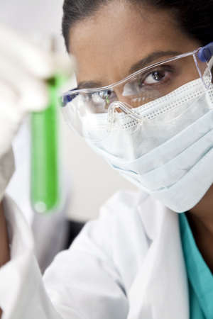 A female Asian medical or scientific researcher or doctor looking at a test tube of a green solution in a laboratory.の写真素材