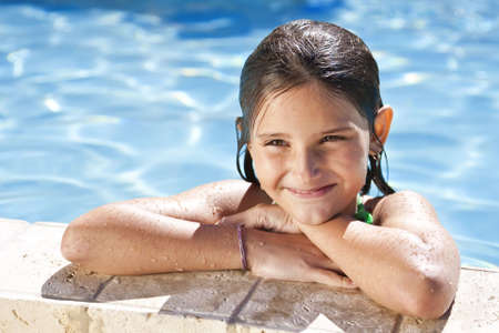 A happy young girl relaxing on the side of a swimming pool and smilingの写真素材