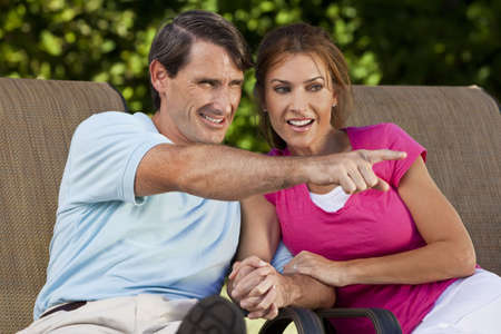 Portrait shot of an attractive, successful and happy middle aged man and woman couple in their thirties, sitting togther holding hands and smiling while the man is pointing off camera.の写真素材