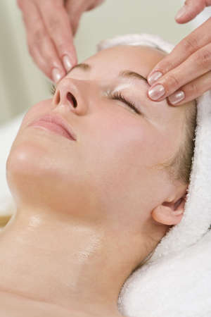 A young woman relaxing at a health and beauty spa while having a head massage or facial treatmentの写真素材