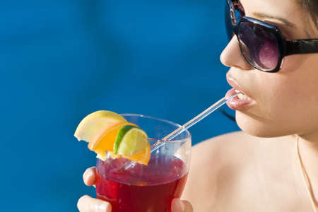 Stunningly beautiful young latina Hispanic woman drinking a red cocktail by a blue swimming poolの写真素材