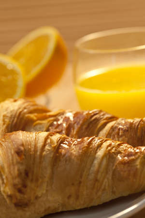 A healthy continental breakfast of croissant pastries, orange juice, oranges Illuminated with golden early morning sunshine.の写真素材