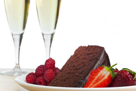 A plate of chocolate cake, raspberries and sliced strawberries with two flute glasses of champagne in the background.の写真素材