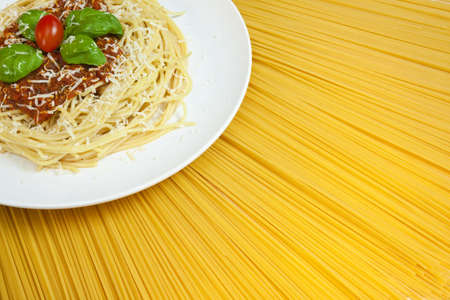 Plate of Spaghetti Bolognese with basil garnish, grated Parmesan cheese and plum tomato displayed on a fan arrangement of dried spaghetti pasta giving a sunshine concept.の写真素材