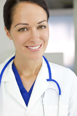 An attractive smiling female doctor wearing a white coat and stethoscope in a hospital.の写真素材