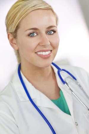 An attractive smiling female doctor wearing a white coat and stethoscope in a hospital.の写真素材