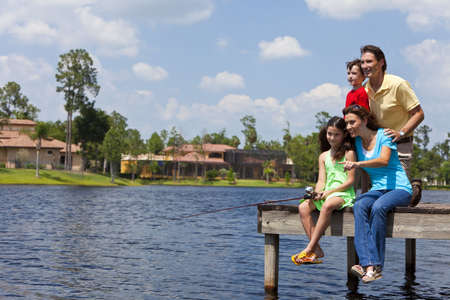A modern family of mother, father, children, son and daughter fishing in a lake off a jetty on a sunny dayの写真素材