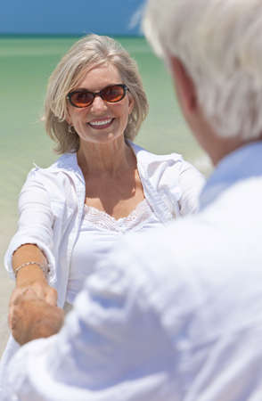 Happy senior man and woman couple dancing and holding hands on a deserted tropical beach with bright clear blue skyの写真素材