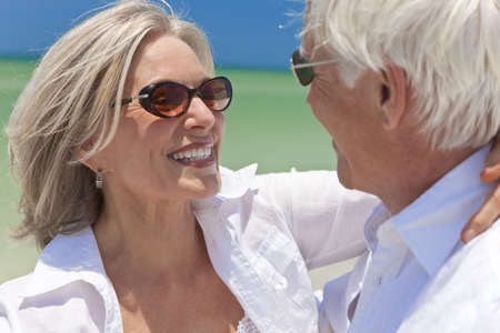 Happy senior man and woman couple dancing and holding hands on a deserted tropical beach with bright clear blue skyの写真素材