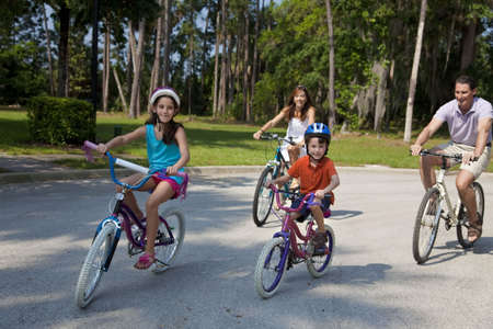 A modern family of two parents and two children, a boy and a girl, cycling together.の写真素材