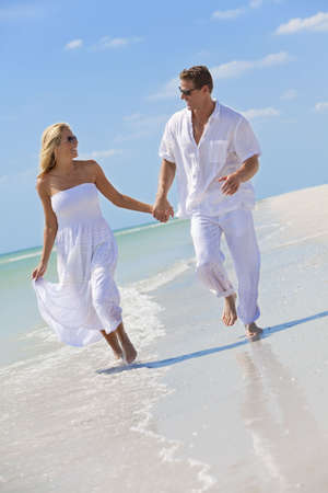 Happy young man and woman couple running, laughing and holding hands on a deserted tropical beach with bright clear blue skyの写真素材