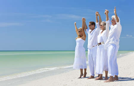 Two couples, generations of a family together holding hands and racing their arms in celebration on a deserted tropical beachの写真素材