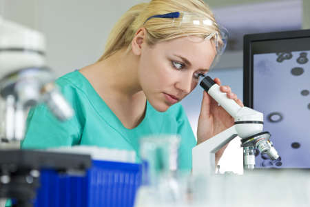 A beautiful female medical or scientific researcher or woman doctor using her microscope in a laboratoryの写真素材