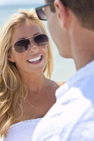 A sexy and attractive man and woman couple wearing sunglasses and having romantic fun laughing in the sunshine at the beachの写真素材