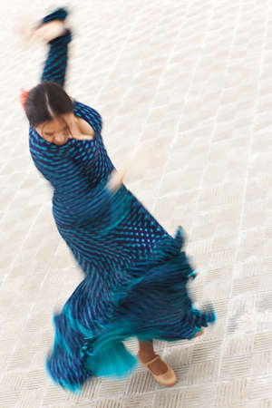 A motion blurred slow shutter speed shot of a woman traditional Spanish Flamenco dancer spinning and dancing in a blue polka dot dressの写真素材