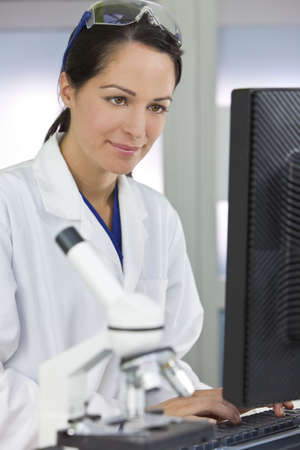 A smiling female medical or scientific researcher or woman doctor using a computer in a laboratory with microscope and other equipment in the foreground.の写真素材