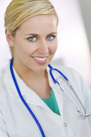 An attractive smiling female doctor wearing a white coat and stethoscope in a hospital.の写真素材