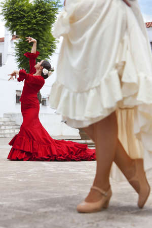 Two women traditional Spanish Flamenco dancers dancing in a town square, the focus is on the dancer in the red dressの写真素材