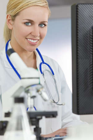 A smiling female medical or scientific researcher or woman doctor using a computer in a laboratory with microscope and other equipment in the foreground.の写真素材