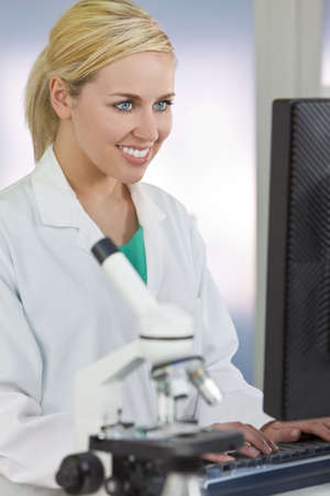 A smiling female medical or scientific researcher or woman doctor using a computer in a laboratory with microscope and other equipment in the foreground.の写真素材
