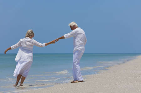 Happy senior man and woman couple dancing and holding hands on a deserted tropical beach with bright clear blue skyの写真素材