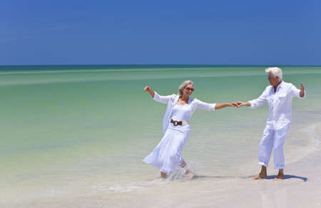 Happy senior man and woman couple dancing and holding hands on a deserted tropical beach with bright clear blue skyの写真素材