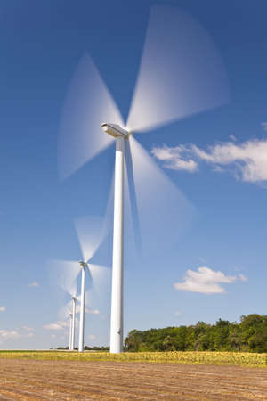 A farm of wind turbines or windmills providing alternative sustainable green energy, situated in a field of sunflowersの写真素材