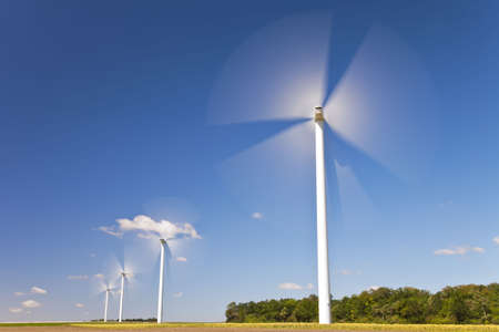 A farm of wind turbines or windmills providing alternative sustainable green energy, situated in a field of sunflowersの写真素材