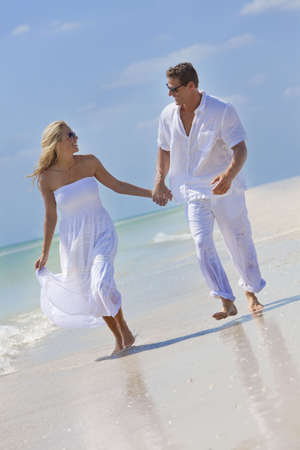 Happy young man and woman couple running, laughing and holding hands on a deserted tropical beach with bright clear blue skyの写真素材