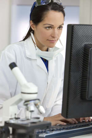 A smiling female medical or scientific researcher or woman doctor using a computer in a laboratory with microscope and other equipment in the foreground.の写真素材