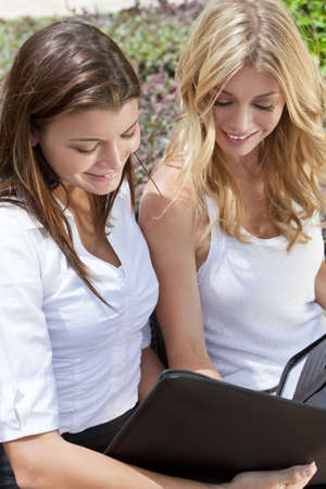 Two attractive young businesswomen or female executives meeting outside looking at a folderの写真素材