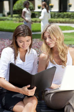 Two attractive you businesswomen or female executives meeting outside with laptop computer and folderの写真素材