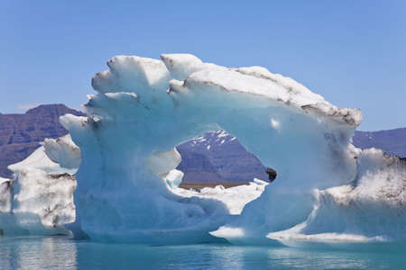 A glacial iceberg with a hole through its center floating on the Iceberg Lagoon, Jokulsarlon, Icelandの写真素材
