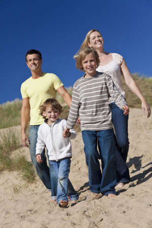 A happy family of mother, father and two sons, walking holding hands and having fun in the sand dunes of a sunny beachの写真素材