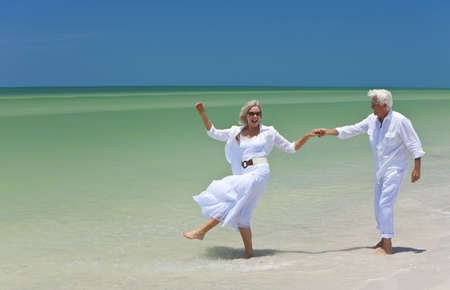 Happy senior man and woman couple dancing and holding hands on a deserted tropical beach with bright clear blue skyの写真素材