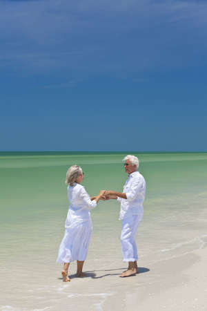 Happy senior man and woman couple dancing and holding hands on a deserted tropical beach with bright clear blue skyの写真素材