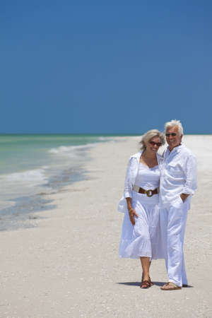 Happy senior man and woman couple together laughing on a deserted tropical beach with bright clear blue sky.の写真素材