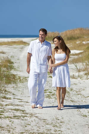 Man and woman romantic couple in white clothes holding hands and walking on a deserted tropical beach with bright clear blue skyの写真素材