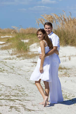 Man and woman romantic happy couple in white clothes walking on a deserted tropical beach with bright clear blue skyの写真素材